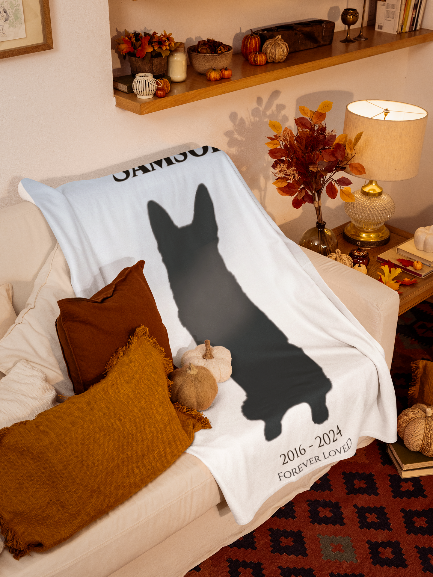 Watercolor pet memorial blanket draped on a sofa in a cozy living room, showing personalized silhouette and dates.
